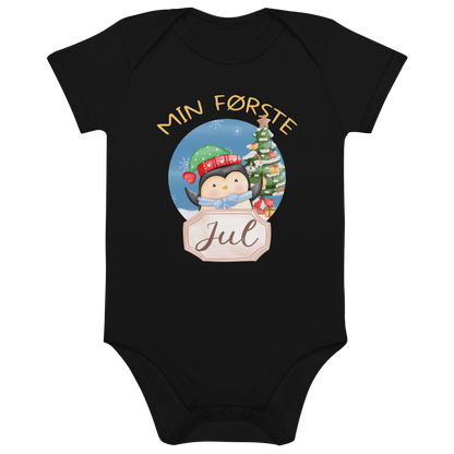 Svart babybody som ligger flatt, med teksten "Min første jul" og figur av en glad pingvin med nisselue og skjerf foran et juletre. Foto.