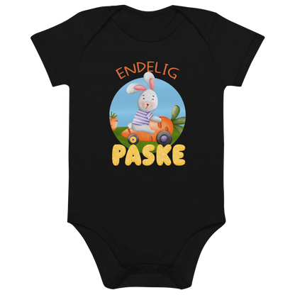 Svart babybody som ligger flatt, med teksten "Endelig påske" og figur av en glad kanin som kjører en gulrotbil. Foto.