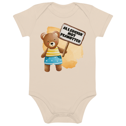 Beige babybody som ligger flatt, med en glad bamse som holder oppe et skilt med teksten "Allergisk mot peanøtter". Foto.