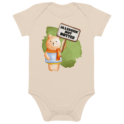 Beige babybody som ligger flatt, med en glad bamse som holder oppe et skilt med teksten "Allergisk mot nøtter". Foto.