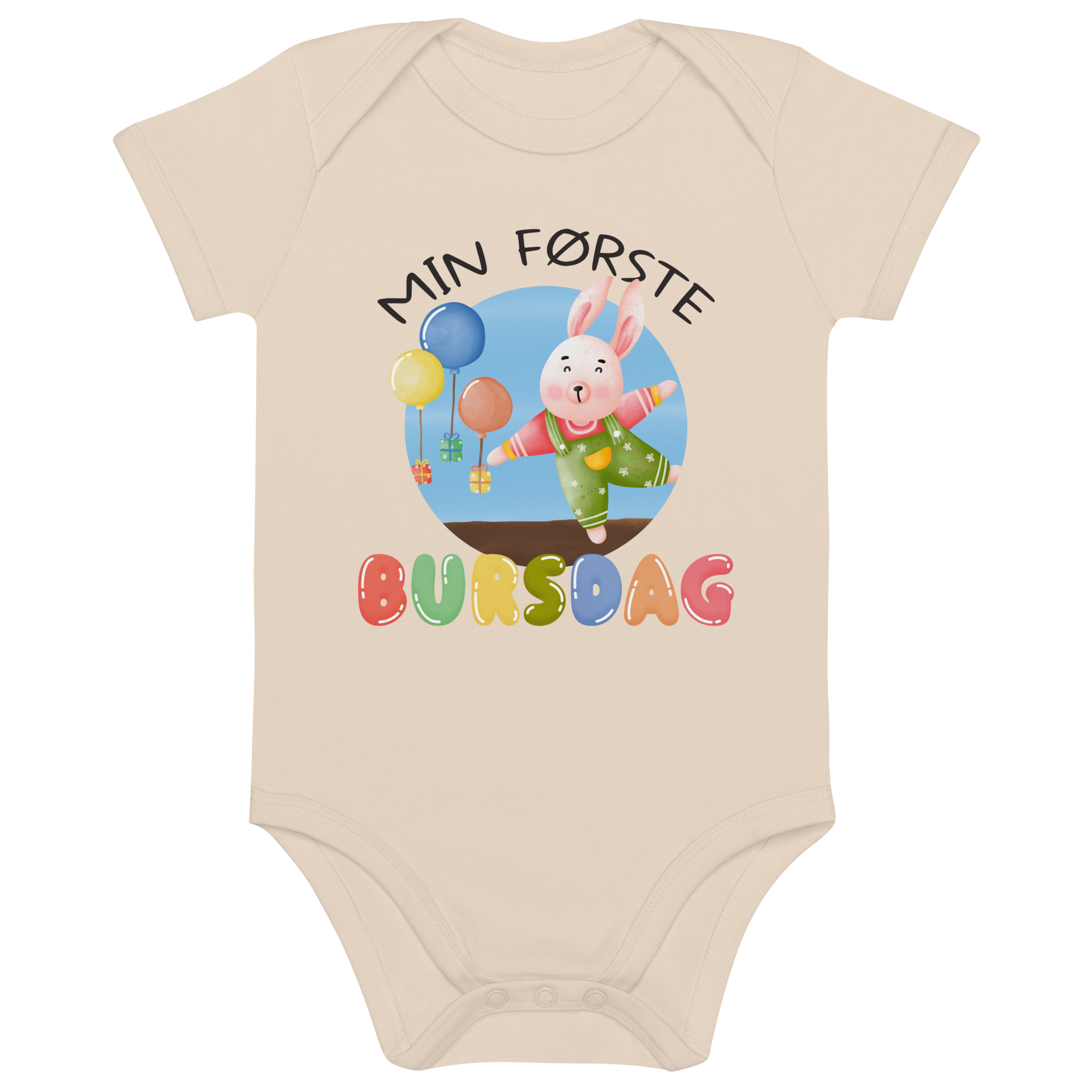 Beige babybody som ligger flatt, med teksten "Min første bursdag" og figur av en glad kanin og gaver som blir holdt oppe i luften av ballonger. Foto.