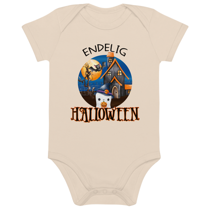 Beige babybody som ligger flatt, med teksten "Endelig halloween" og figur av et søtt spøkelse med heksehatt foran et hus med en stor fullmåne i bakgrunnen. Foto.