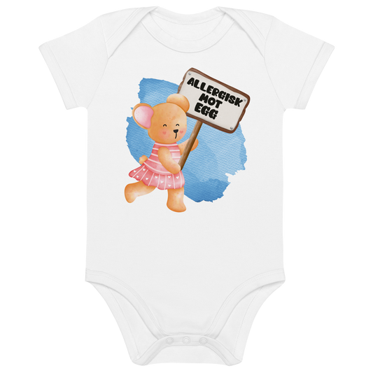Hvit babybody som ligger flatt, med en glad bamse som holder oppe et skilt med teksten "Allergisk mot egg". Foto.