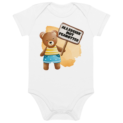 Hvit babybody som ligger flatt, med en glad bamse som holder oppe et skilt med teksten "Allergisk mot peanøtter". Foto.