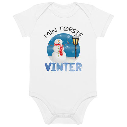 Hvit babybody som ligger flatt, med teksten "Min første vinter" og figur av en glad snømann ved en gammeldags lyktestolpe. Foto.