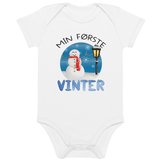 Hvit babybody som ligger flatt, med teksten "Min første vinter" og figur av en glad snømann ved en gammeldags lyktestolpe. Foto.