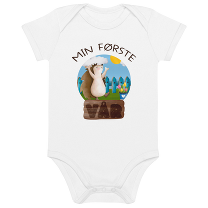 Hvit babybody som ligger flatt, med teksten "Min første vår" og figur av et lykkelig pinnsvin som nyter at varmen kommer tilbake. Foto.