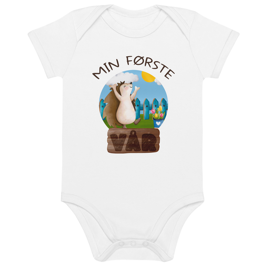 Hvit babybody som ligger flatt, med teksten "Min første vår" og figur av et lykkelig pinnsvin som nyter at varmen kommer tilbake. Foto.