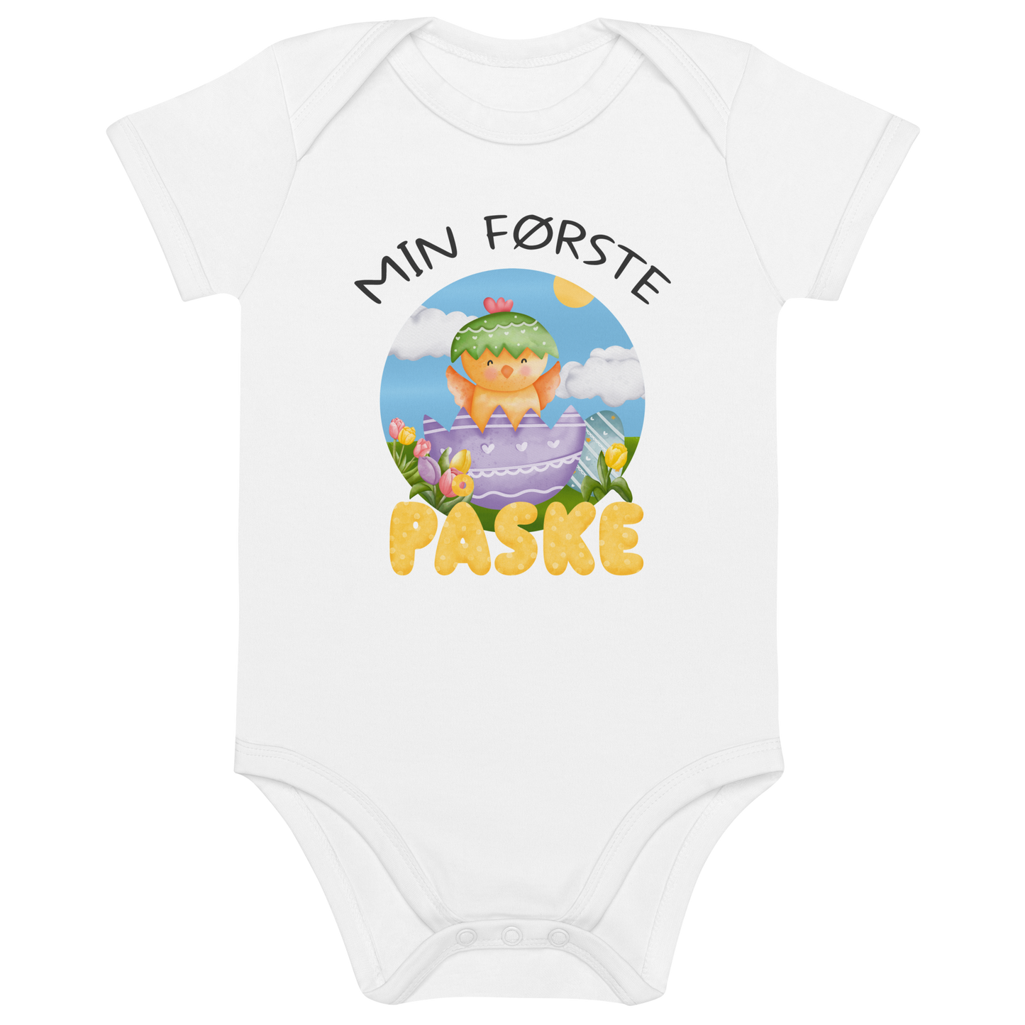 Hvit babybody som ligger flatt, med teksten "Min første påske" og figur av en glad kylling som hopper ut av et påskeegg. Foto.