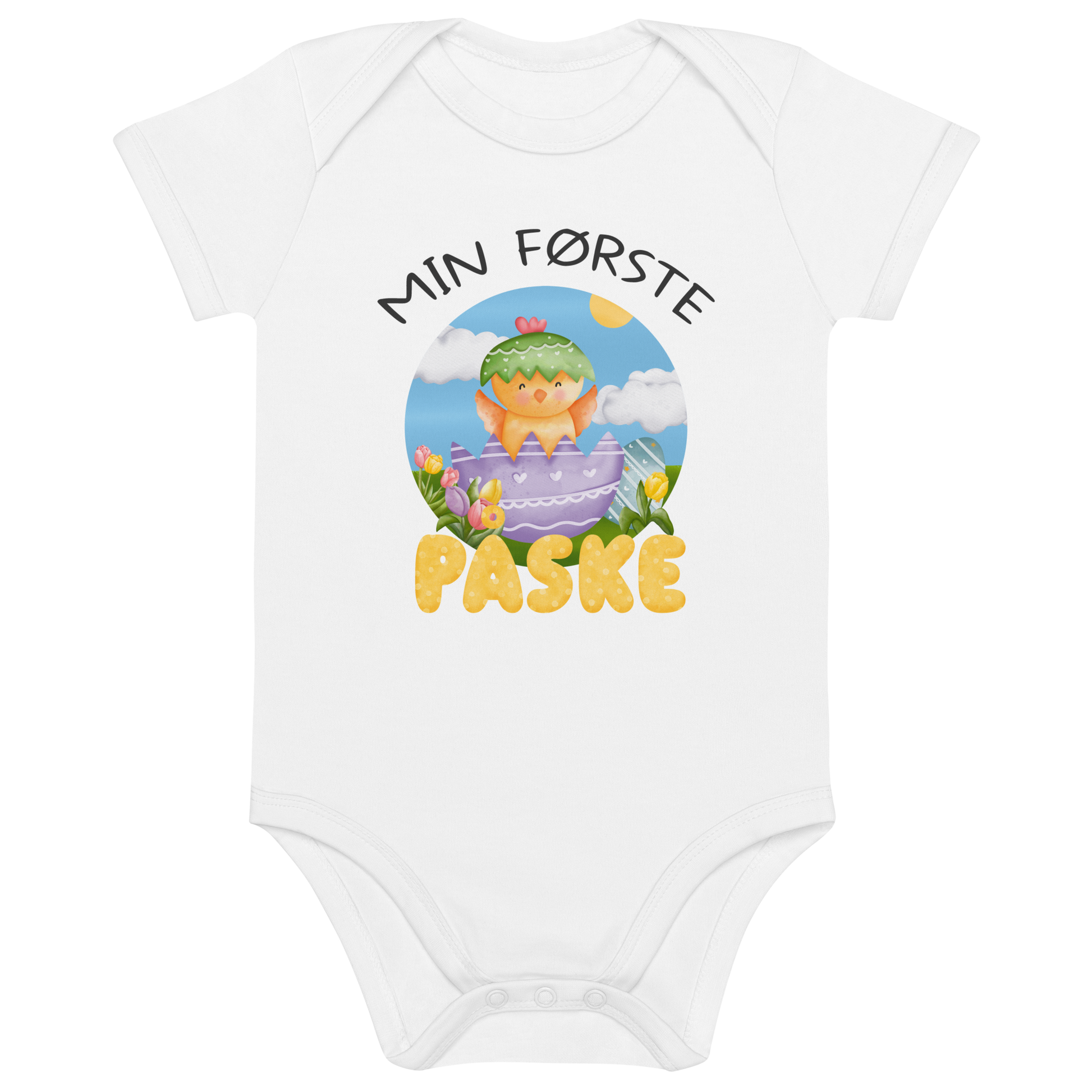 Hvit babybody som ligger flatt, med teksten "Min første påske" og figur av en glad kylling som hopper ut av et påskeegg. Foto.