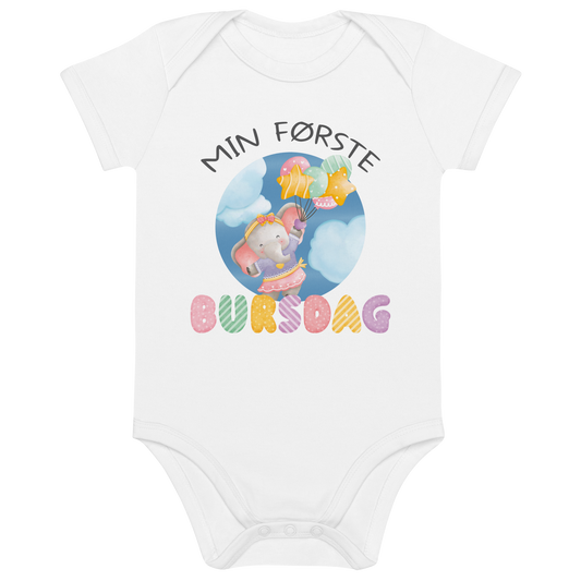 Hvit babybody som ligger flatt, med teksten "Min første bursdag" og figur av en søt og glad elefant som holder flere ballonger og flyr mellom skyene. Foto.