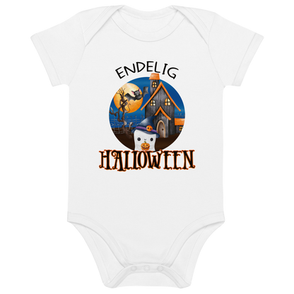 Hvit babybody som ligger flatt, med teksten "Endelig halloween" og figur av et søtt spøkelse med heksehatt foran et hus med en stor fullmåne i bakgrunnen. Foto.