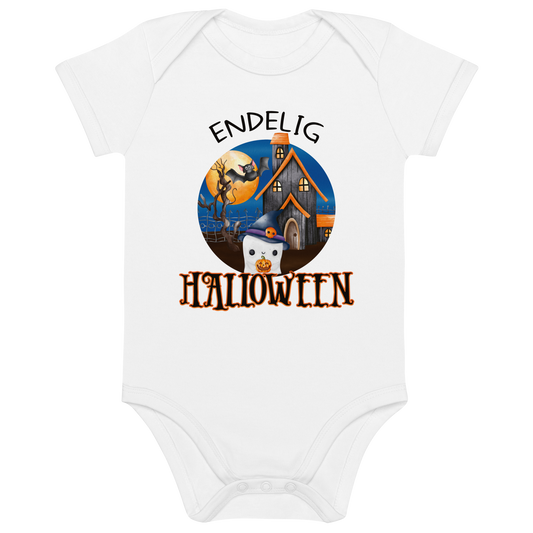 Hvit babybody som ligger flatt, med teksten "Endelig halloween" og figur av et søtt spøkelse med heksehatt foran et hus med en stor fullmåne i bakgrunnen. Foto.