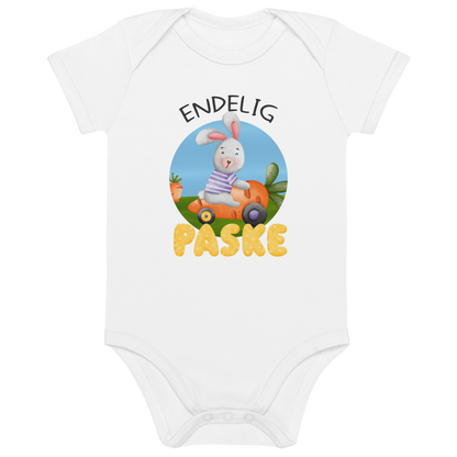 Hvit babybody som ligger flatt, med teksten "Endelig påske" og figur av en glad kanin som kjører en gulrotbil. Foto.