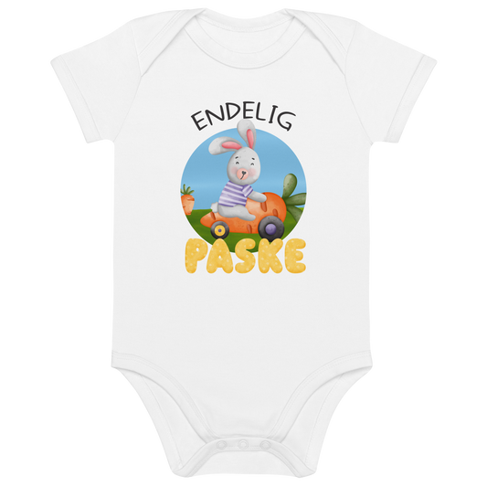 Hvit babybody som ligger flatt, med teksten "Endelig påske" og figur av en glad kanin som kjører en gulrotbil. Foto.