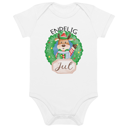 Hvit babybody som ligger flatt, med teksten "Endelig jul" og figur av en søt elg i julete klær med en julekrans rundt seg. Foto.