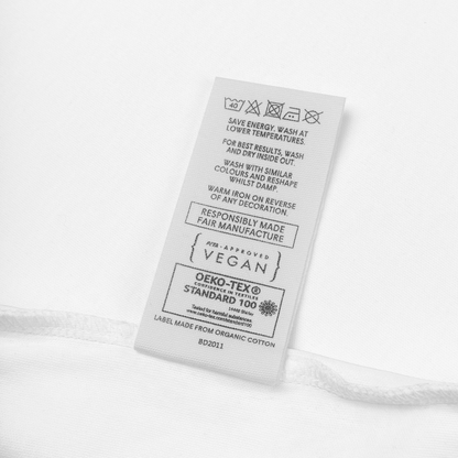 Merkelapp på babybody som viser vaskeinstruksjoner med blant annet at den kan vaskes i maskin på 40 grader, at PETA har godkjent den som vegansk og sertifiseringen OEKO-TEX Standard 100. Foto.