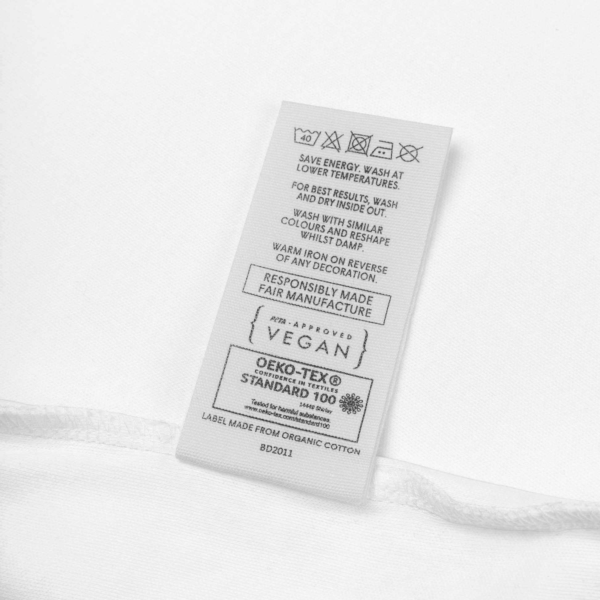 Merkelapp på babybody som viser vaskeinstruksjoner med blant annet at den kan vaskes i maskin på 40 grader, at PETA har godkjent den som vegansk og sertifiseringen OEKO-TEX Standard 100. Foto.