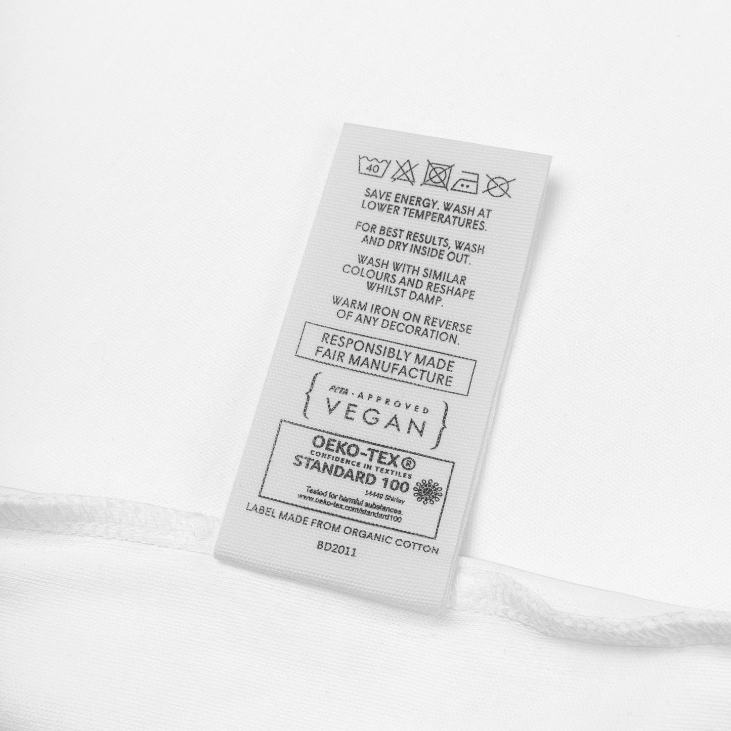Merkelapp på babybody som viser vaskeinstruksjoner med blant annet at den kan vaskes i maskin på 40 grader, at PETA har godkjent den som vegansk og sertifiseringen OEKO-TEX Standard 100. Foto.