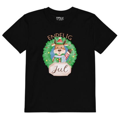 Svart t-skjorte som ligger flatt, med teksten "Endelig jul" og figur av en søt elg i julete klær med en julekrans rundt seg. Foto.