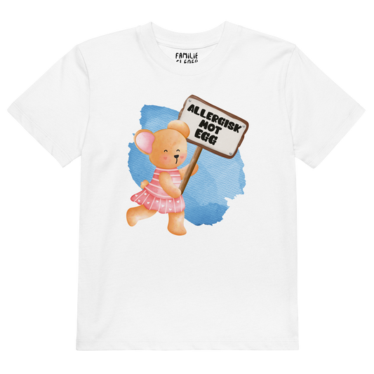 Hvit t-skjorte som ligger flatt, med en glad bamse som holder oppe et skilt med teksten "Allergisk mot egg". Foto.