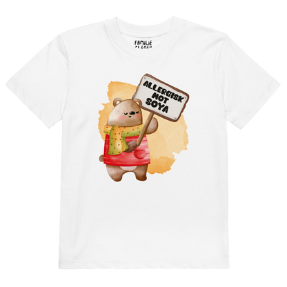 Hvit t-skjorte som ligger flatt, med en glad bamse som holder oppe et skilt med teksten "Allergisk mot soya". Foto.