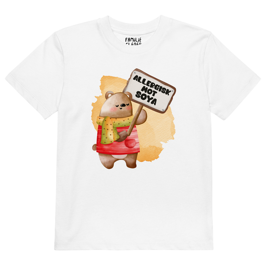 Hvit t-skjorte som ligger flatt, med en glad bamse som holder oppe et skilt med teksten "Allergisk mot soya". Foto.