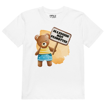 Hvit t-skjorte som ligger flatt, med en glad bamse som holder oppe et skilt med teksten "Allergisk mot peanøtter". Foto.