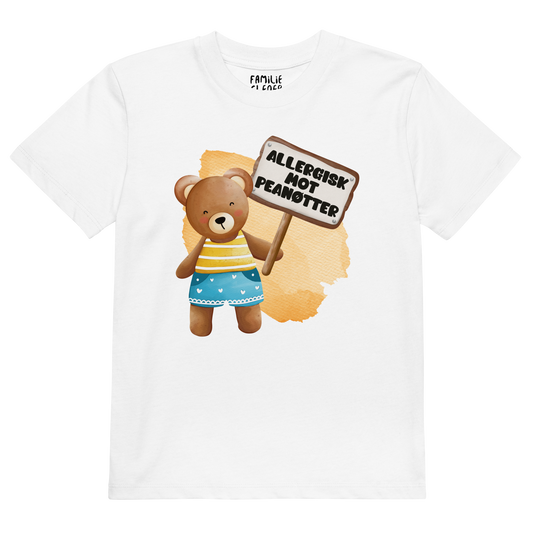 Hvit t-skjorte som ligger flatt, med en glad bamse som holder oppe et skilt med teksten "Allergisk mot peanøtter". Foto.