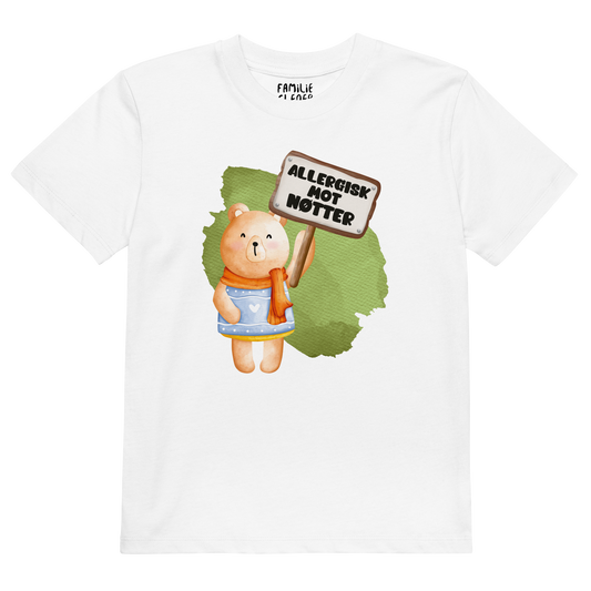 Hvit t-skjorte som ligger flatt, med en glad bamse som holder oppe et skilt med teksten "Allergisk mot nøtter". Foto.