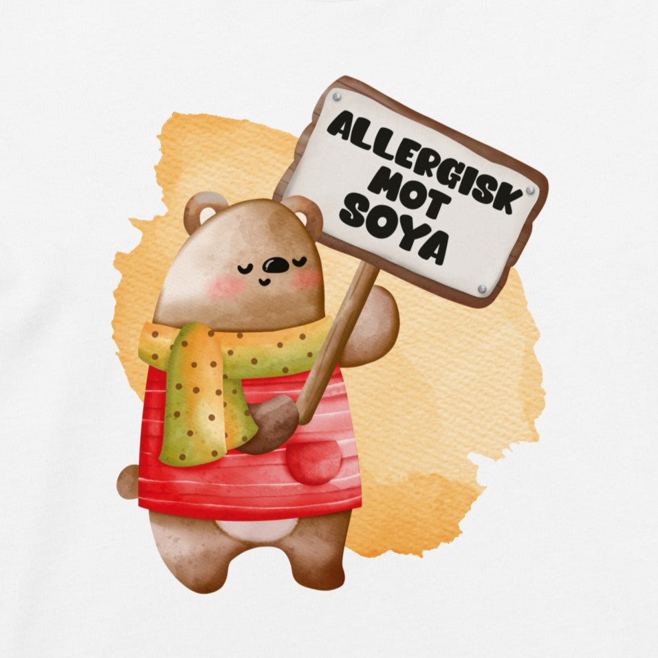 En glad bamse som holder oppe et skilt med teksten "Allergisk mot soya". Foto av motivet trykket på tøy.