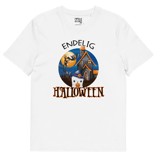 Hvit t-skjorte som ligger flatt, med teksten "Endelig halloween" og figur av et søtt spøkelse med heksehatt foran et hus med en stor fullmåne i bakgrunnen. Foto.