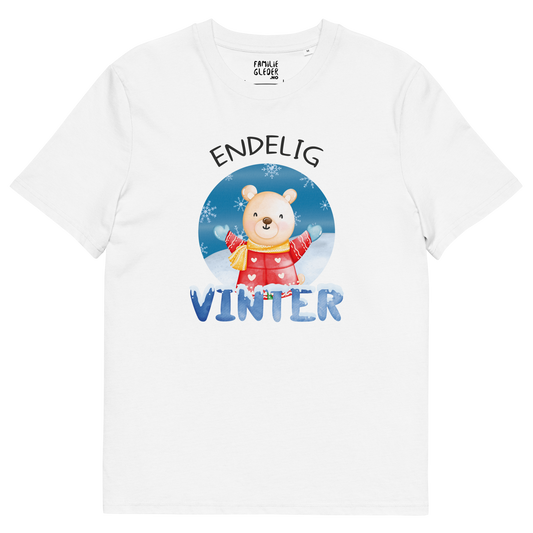 Hvit t-skjorte som ligger flatt, med teksten "Endelig vinter" og figur av en lykkelig bamse i vinterklær som nyter snøen. Foto.