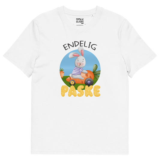 Hvit t-skjorte som ligger flatt, med teksten "Endelig påske" og figur av en glad kanin som kjører en gulrotbil. Foto.